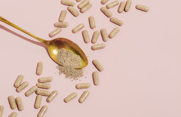 Picture is a pink background with a spoon that is surrounded by capsules and the spoon holds some of the powder from a capsule.