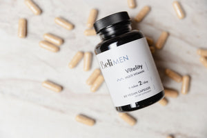 The picture is showing a bottle of Beli Vitality for Men on a counter with capsules surrounding the bottle.