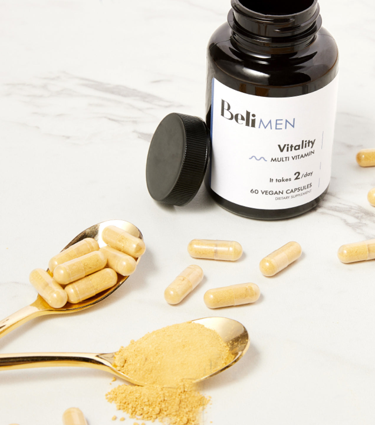 Beli Vitality for Men on a table with some capsules surrounding the bottles. There are two spoons with some capsules on them and some powder from the capsule.
